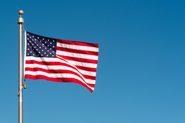 Fototapeta premium Picturesque perfect American flag blowing in the breeze over sky blue background with copy space 