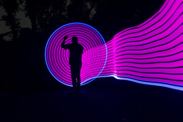 Naklejka premium One person standing alone against a Colourful circle light painting as the backdrop