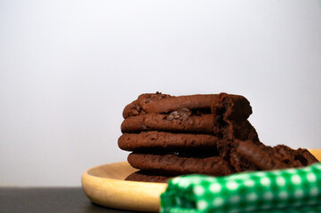 Chocolate cookies are placed in a wooden tray with a green cloth placed over a black background.