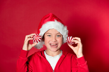 Boy with red Christmas ornament wearing Christmas hat in front of red background celebrating Christmas