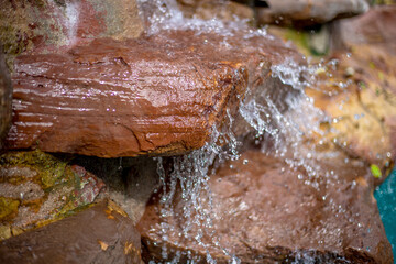 Waterfall blurred background That flows from the rocks, the garden decoration at the swimming pool is seen in the resort or hotel, allowing tourists to swim during the day.