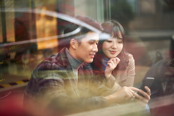 young asian couple sitting on ground looking at cellphone