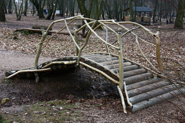 In the spring park with the fallen-down gray leaves there is a small original wooden bridge through a flute.