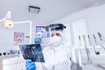 Patient pov in dental office looking at dentist holding radiography dressed in protective gear during covid-19. Dental specialist wearing protective hazmat suit against coroanvirus showing radiography