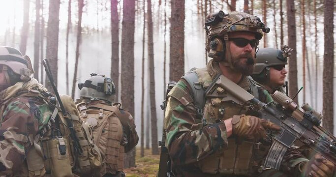 Four Fully Equipped Middle - Aged Soldiers Wearing Camouflage Uniform, They're in Shooting Ready Stance, Aiming Rifles. Military Operation in Action, Squad crouching in Dense Forest.