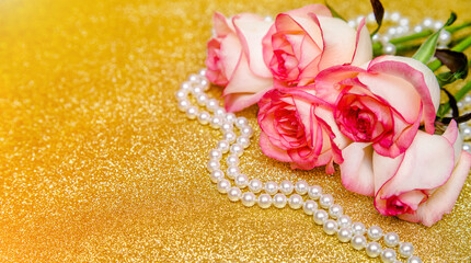Pink rose and pearl necklace on a shiny gold background
