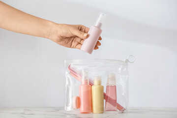 Female hand and bag with travel bottles of body care cosmetics on light background