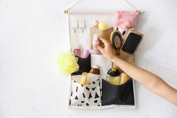 Female hand and hanging pocket organizer with travel kit on light background