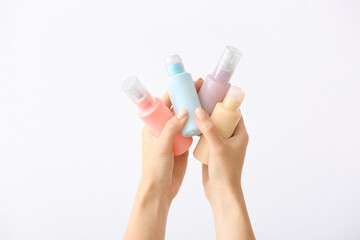 Female hands and travel bottles with body care cosmetics on white background