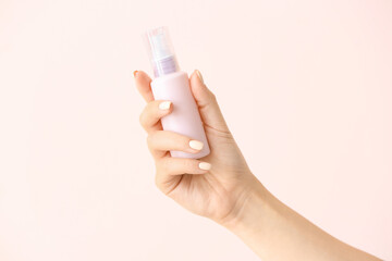 Female hand and travel bottle with body care cosmetics on light background