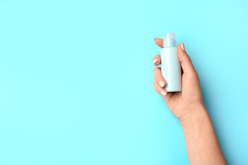 Female hand and travel bottle with body care cosmetics on color background