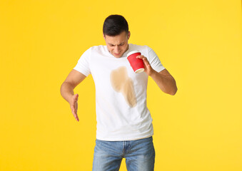 Stressed young man with coffee stains on his t-shirt on color background - obrazy, fototapety, plakaty