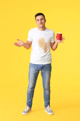 Confused young man with coffee stains on his t-shirt on color background