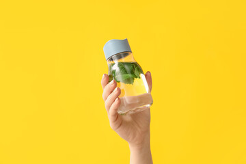 Female hand and bottle of mint infused water on color background