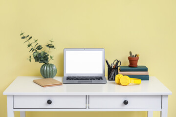 Modern workplace with laptop, houseplant and headphones near color wall