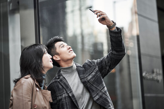 young asian couple taking a selfie outdoors with cellphone