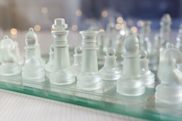 Transparent glass chess pieces on a white wooden table.