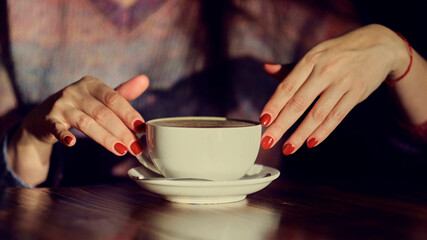 Fototapeta na wymiar woman hands with latte on a wood table. woman with red nails holds coffee in her hands.