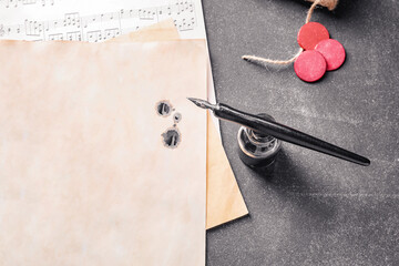 Nib pen, inkwell and musical note sheets on black table