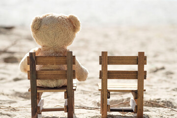 Teddy bear sit on wooden chair with sea view. Love and relationship concept. Beautiful white sandy...