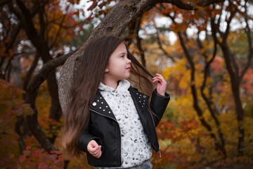 Cute kid girl 4-5 year old wearing sweater and jacket in park. Looking at camera. Autumn season. Childhood.