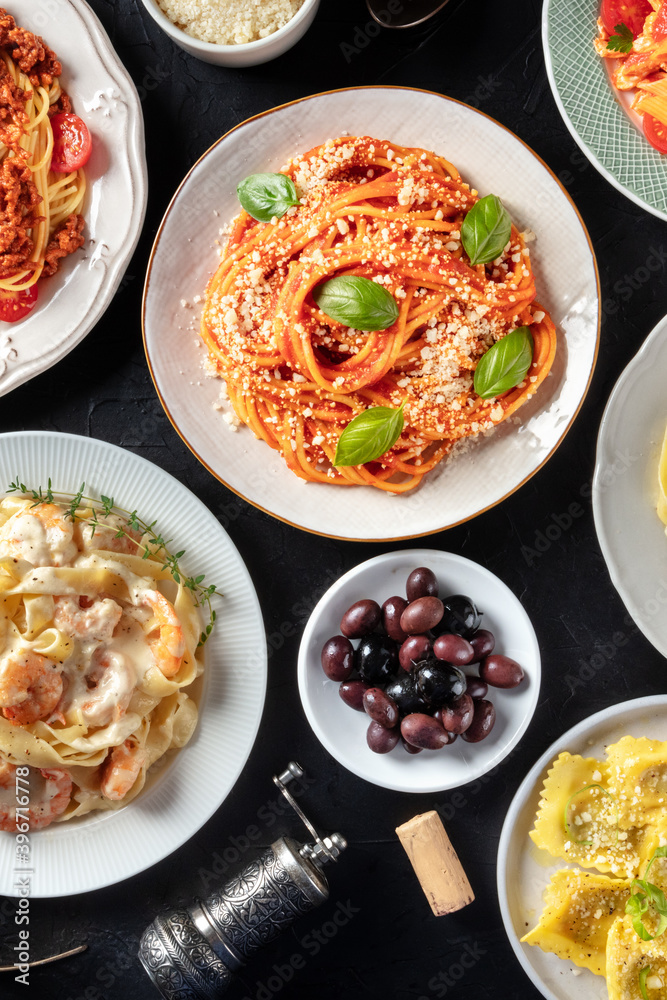 Wall mural italian food, shot from above on a black background. spaghetti with basil, olives, wine cork, raviol