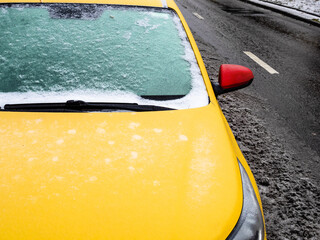 frozen windshield of yellow car parked on dirty city road after freezing rain on cold autumn day