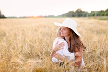 Caucasian beautiful mother hugs her child son in the summer wheat field at sunset, summer and harvest, rest in the village