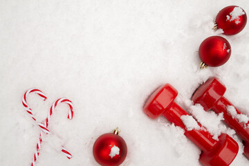 Red dumbbells, decorative baubles ornaments and candy canes on a white snow for Christmas. Healthy...
