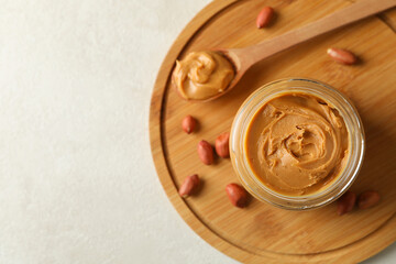 Board with peanut, spoon and jar with peanut butter on white background
