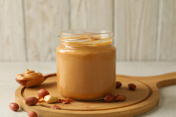 Board with peanut, spoon and jar with peanut butter on white table