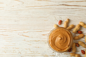 Peanut and bowl with peanut butter on wooden background