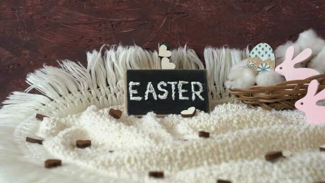 Easter concept. On a knitted napkin is a board with Easter and a basket with eggs and pink rabbits
