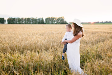 Fototapeta na wymiar Caucasian beautiful mother hugs her child son in the summer wheat field at sunset, summer and harvest, natural products and relaxation in the countryside, motherhood