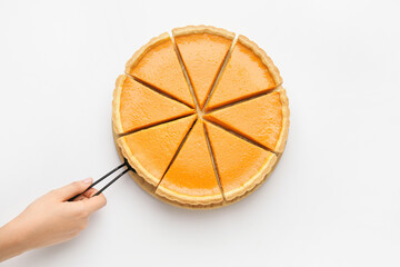 Female hand with spatula and tasty cut pumpkin pie on white background
