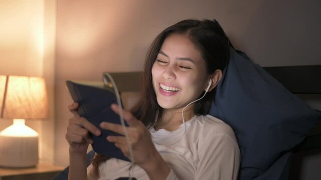 A young woman is using tablet , watching movies or video call to her friends or family  in her bedroom , night Light 