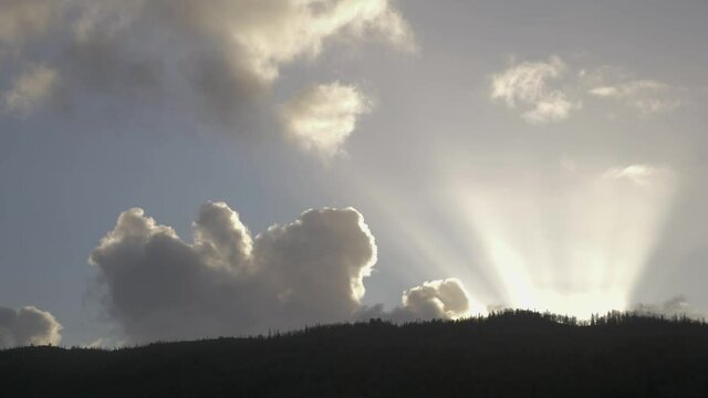 Heavenly sun behind hill lighting up clouds on the blue sky at daytime in Norway