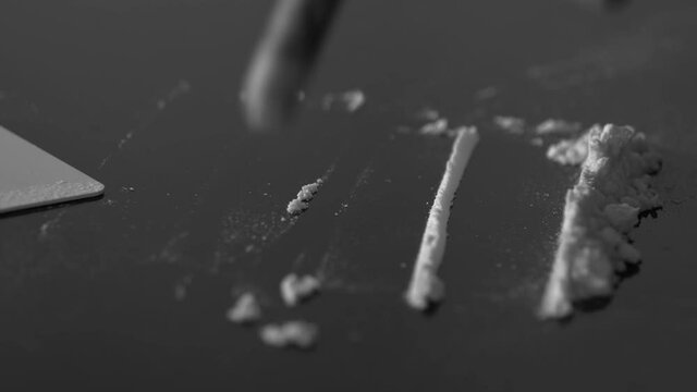 A rolled banknote snorting a line of cocaine powder. Drug Abuse. Sniffing Cocaine lines. White powder on black table. Macro shot.