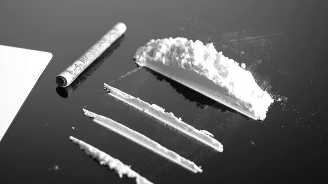 Lines of cocaine and a dollar bill. Cocaine lines shots on a black table glass. Cocaine powder, Credit card, close up, toned. Drug abuse concept. White poder on black table