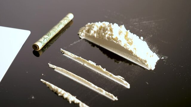 Lines of cocaine and a dollar bill. Cocaine lines shots on a black table glass. Cocaine powder, Credit card, close up, toned. Drug abuse concept. White poder on black table