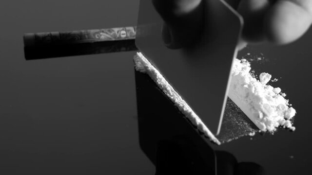 A rolled banknote snorting a line of cocaine powder. Drug Abuse. Sniffing Cocaine lines. White powder on black table. Macro shot.