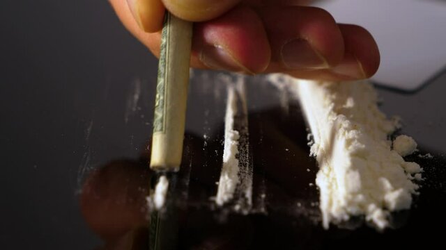 A rolled banknote snorting a line of cocaine powder. Drug Abuse. Sniffing Cocaine lines. White powder on black table. Macro shot.