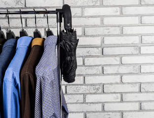 Shirts, a warm sweater and an umbrella are hanging on a hanger. Men's wardrobe. Style and fashion. Background and texture.