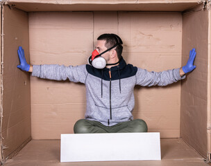 man in a protective mask sits by a cardboard box with his hands to the sides