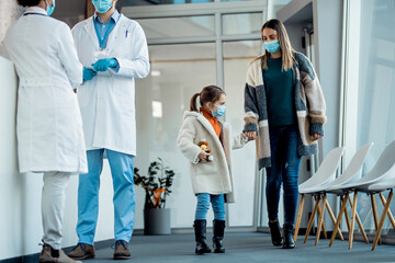 Mother and daughter with face masks holding hands while coming to the hospital.