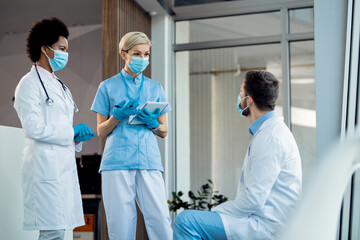 Obraz premium Group of healthcare workers wearing face masks while communicating in a hallway at the hospital.
