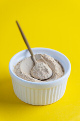 Sunflower lecithin in a bowl with a spoon on a yellow background.