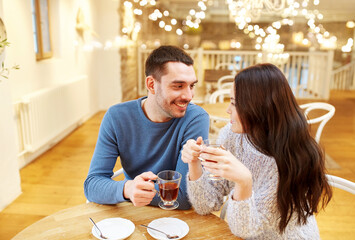 people, valentine's day and dating concept - happy couple drinking tea at cafe or restaurant over festive lights