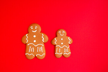 Two tasty homemade Christmas gingerbread mans with sugar glaze on bright red festive background with copy space. Close up