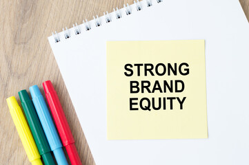 the inscription on the yellow sheet for notes text STRONG BRAND EQUITY which is attached to the notebook on the table.
